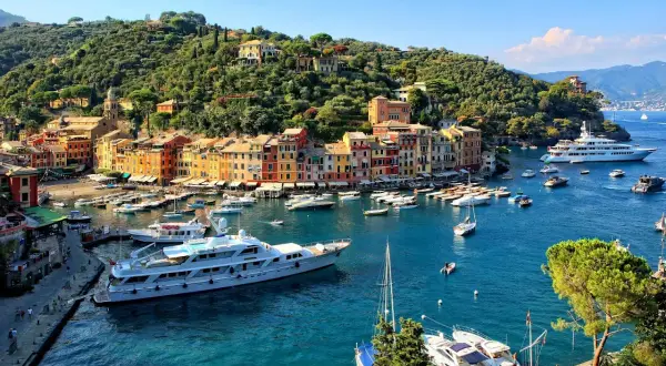 Portofino: cosa vedere? Un incantevole borgo ligure con case colorate, un porto pieno di yacht e una collina verdeggiante.