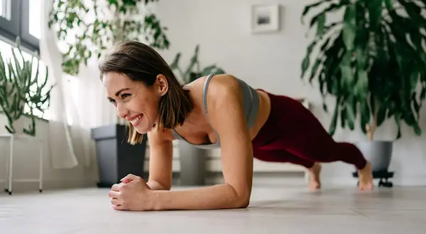 Femme souriante en position de planche, un excellent exercice ventre pour renforcer son corps à la maison.