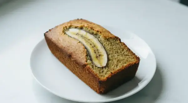 Pyszny chlebek bananowy z plasterkiem banana na wierzchu, podany na białym talerzyku.