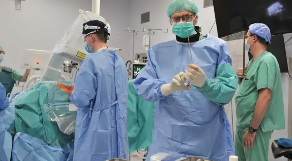 Chirurdzy w sterylnych strojach przygotowują się do operacji kręgosłupa lędźwiowego. Jeden z nich trzyma narzędzie, gotowy do precyzyjnego działania.