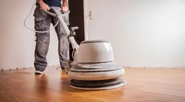 Un ouvrier utilise une ponceuse pour appliquer de l'huile sur un parquet en bois.