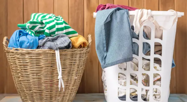 Zwei Wäschekörbe, einer aus Weide, der andere weiß, gefüllt mit Kleidung. Grüne und weiße Streifen, Blau und Gelb. Die Frage ist, welche Farben zusammen waschen.