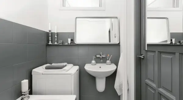 Baño moderno con azulejos grises, lavadora y lavabo. Un ejemplo de reformas de baños antes y después, con un estilo minimalista y funcional.