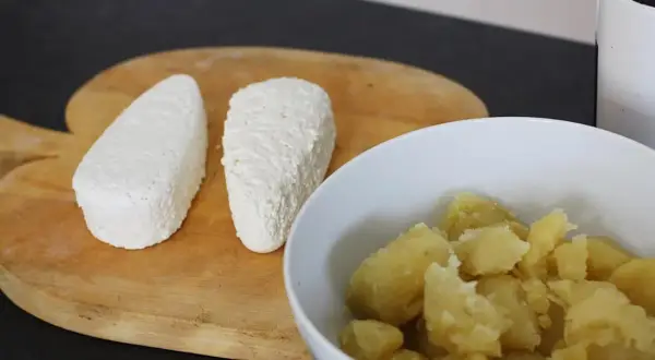 Dwa białe, podłużne kawałki sera leżą obok miski z ugotowanymi ziemniakami. Idealne kopytka z serem czekają na przygotowanie.