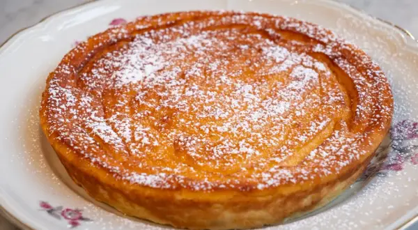 Migliaccio napoletano ricetta della nonna, dorato e cosparso di zucchero a velo, su un piatto decorato.