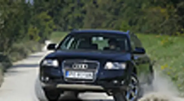 Ciemny Audi allroad pokonuje piaszczystą drogę, wzbijając kurz.