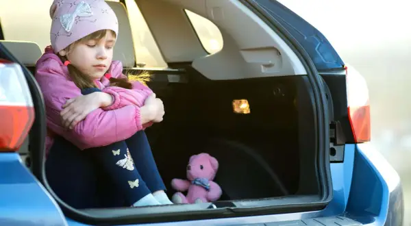 Traurige Kinder im Kofferraum, nur ein Teddybär als Gesellschaft.