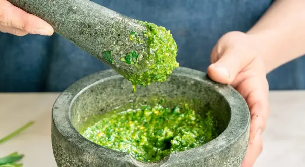 Frische Kräuter werden im Mörser zerstoßen, um ein leuchtend grünes Pesto zuzubereiten. Perfekt für einfache Pesto Rezepte.