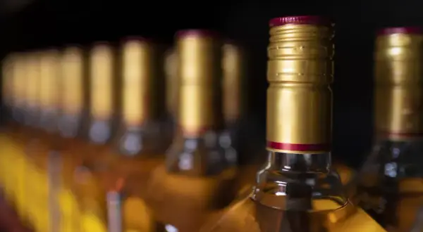 Rząd butelek z alkoholem, przypominający o limitach w Islandii. Złote zakrętki i bursztynowy płyn.