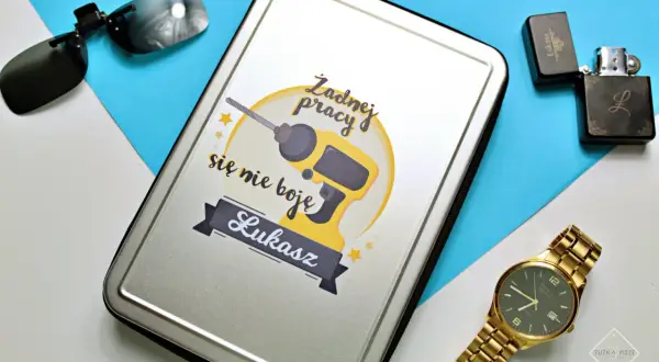 Prezent na dzień chłopaka dla Łukasza: metalowe pudełko z wiertarką i napisem "Żadnej pracy się nie boję", obok okulary, zapalniczka i złoty zegarek.