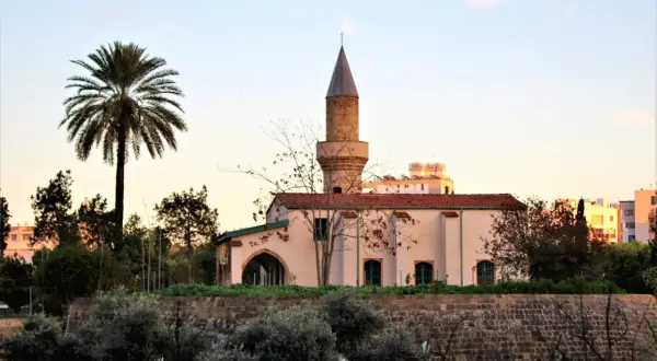 Minaret i meczet w Nikozji, stolicy Cypru, na tle palmy i zachodzącego słońca.