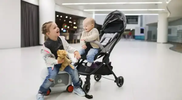 Dzieci w wózku dziecięcym Wizzair, starsza siostra trzyma misia, młodsza siedzi w wózku.