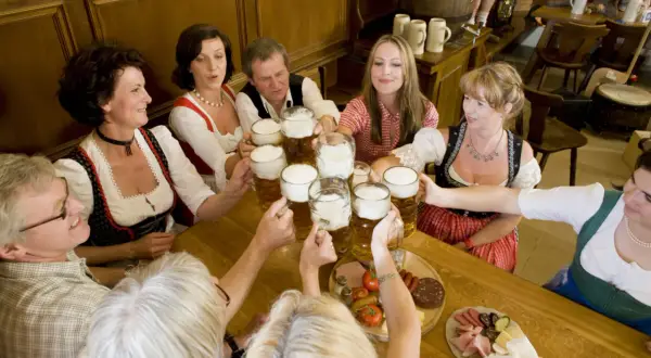 Bayrische Gemütlichkeit: Menschen in Tracht stoßen mit Bierkrügen an. Bier ist ein Grundnahrungsmittel in Bayern.