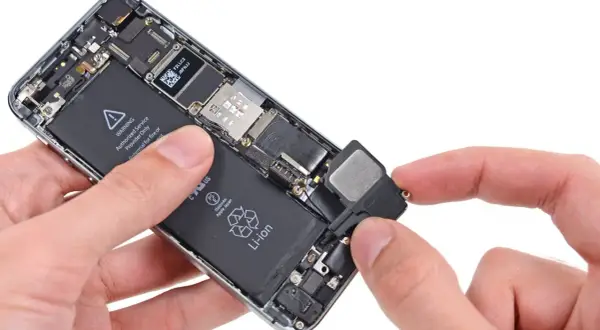 Dłonie trzymają otwarty telefon, wyjmując głośnik. Dowiedz się, jak sprawdzić głośnik w telefonie, gdy masz dostęp do jego wnętrza.