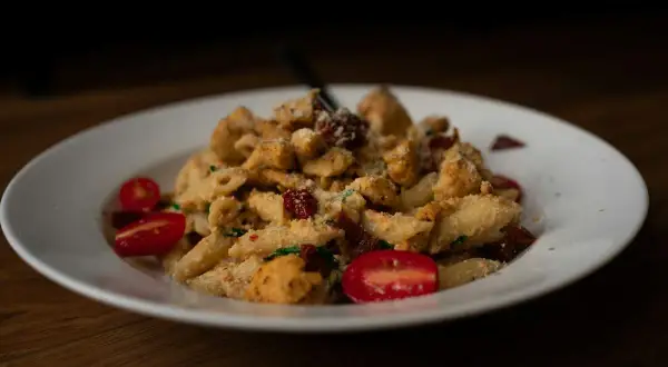 Penne z kurczakiem, suszonymi pomidorami i parmezanem, podane z pomidorkami koktajlowymi. Kremowy sos na bazie serka typu Philadelphia idealnie otula makaron.