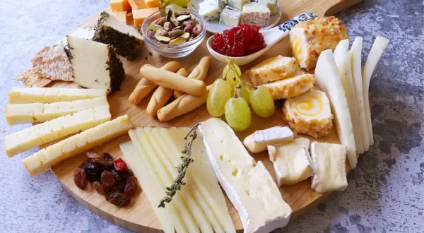 Una deliciosa presentación tabla de quesos con variedad de quesos, uvas, frutos secos y panecillos.