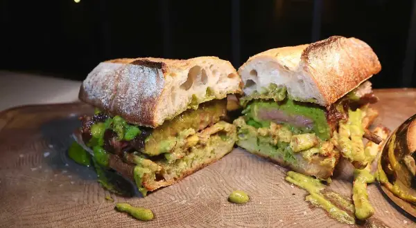 En saftig steak sandwich med avokado och en grön sås, upplagd på en träskärbräda.
