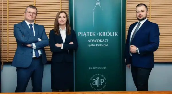 Trzy osoby w garniturach stoją przed zielonym banerem kancelarii prawniczej Piątek-Krolik.