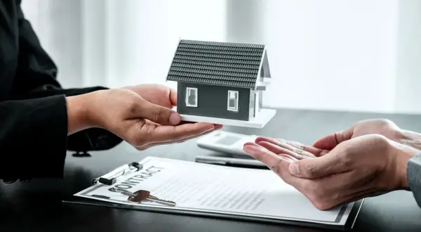Manos entregan maqueta de casa sobre contrato. Posible exención IRPF venta vivienda heredada.