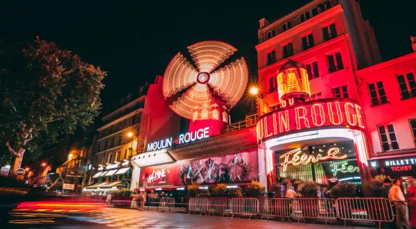 Nocny Paryż rozświetlony neonami Moulin Rouge. Wirujący wiatrak i czerwone światła tworzą magiczną atmosferę.