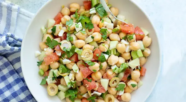 Ensalada de garbanzos fresca con tomate, pepino, aceitunas y perejil, lista para disfrutar.