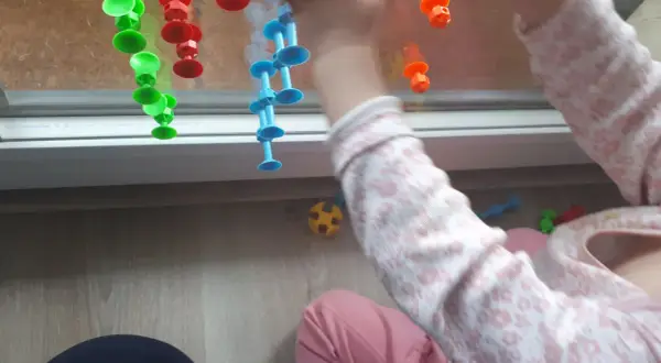 Roczne dziecko bawi się kolorowymi przyssawkami na oknie, tworząc kreatywne zabawy.
