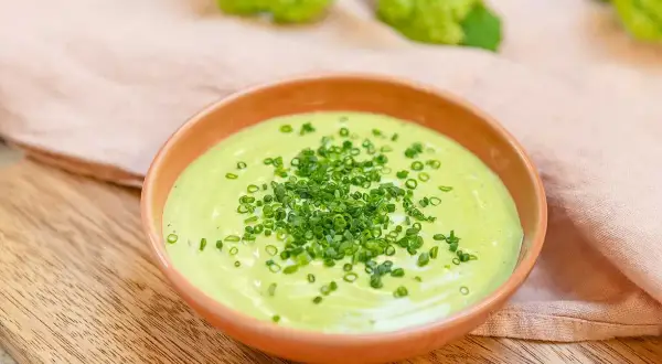 Grön, krämig salsa verde toppad med finhackad gräslök i en skål på en träskärbräda.