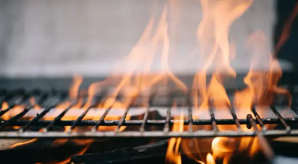 Płomienie tańczą nad rusztem, pokazując, jak rozpalic grilla. Drewno żarzy się, tworząc idealne warunki do grillowania.