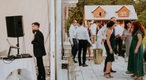 DJ przygotowuje się do przyjęcia weselnego w lesie. Goście bawią się na tarasie przed domem.