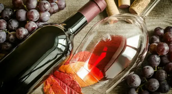 Uva Sangiovese, vitigno del Brunello di Montalcino, accompagna una bottiglia e un calice di vino rosso, su un tavolo di legno rustico.