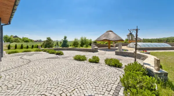 Piękny ogród z krętymi ścieżkami wyłożonymi kostką granitową, altaną krytą strzechą i basenem pod kopułą.