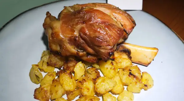 Stinco di maiale succulento e dorato, servito con patate arrosto croccanti e profumate al rosmarino.