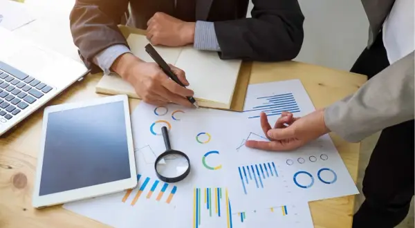 Deux personnes analysent des graphiques et des données pour un audit énergétique. Un ordinateur portable et une tablette sont sur la table.