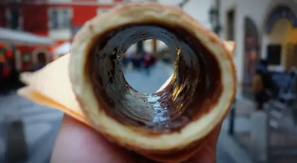 Trdelník z czekoladą, jeden z pysznych czeskich przysmaków, widziany przez jego wnętrze na tle ulicy.