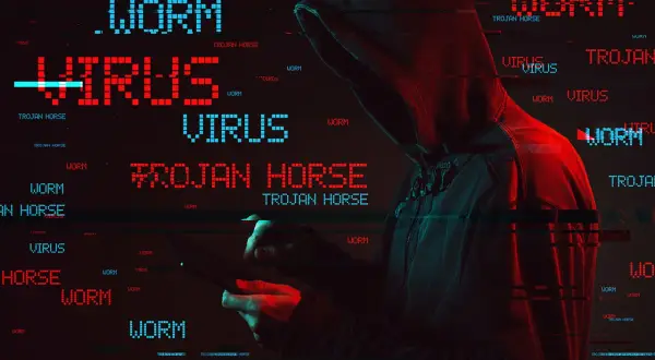 Haker w kapturze, otoczony przez migoczące napisy "WORM", "VIRUS" i "TROJAN HORSE". To pokazuje, co to trojan - złośliwe oprogramowanie udające coś pożytecznego.