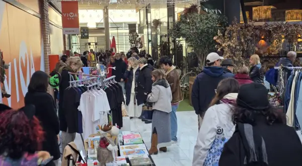 Gente comprando en un rastro de Zaragoza. Hay ropa colgada en percheros y puestos con libros y adornos.
