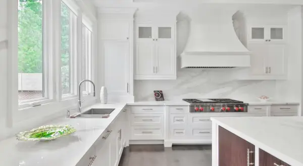 Cocina moderna blanca con encimeras de cuarzo. Muebles de cocina de melamina con tiradores plateados. Campana extractora y estufa profesional.