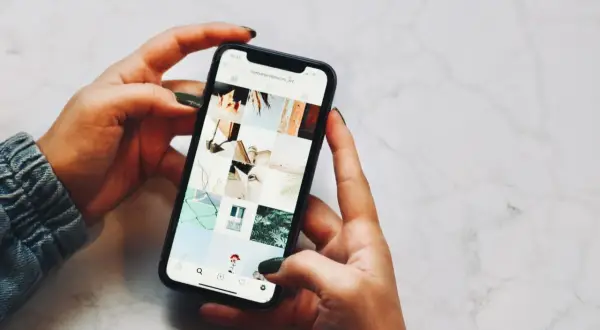 Dłonie trzymające telefon, na ekranie widoczny profil Instagrama z moimi pracami. Niestety, moje urządzenie iPhone niedostępne.