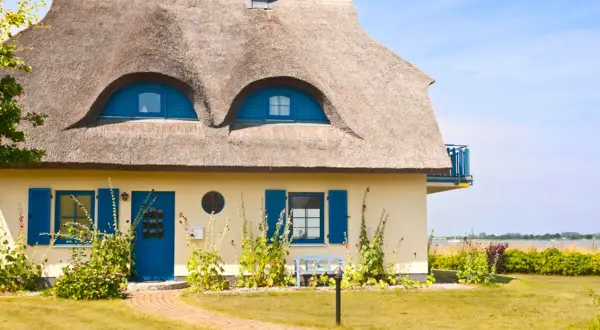 Charmantes Haus mit Reetdach und blauen Akzenten. Ein Blick auf die Frage: was kostet ein reetdach?