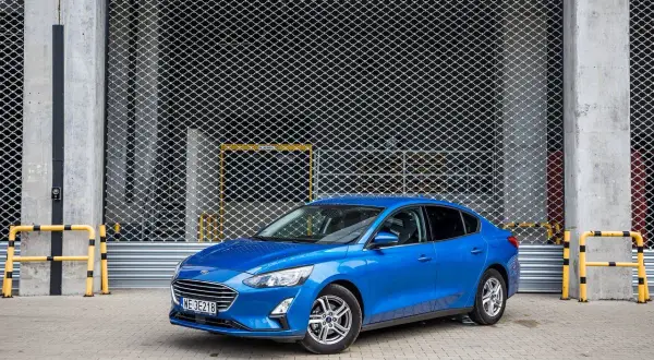 Niebieski Ford Focus 1.0 EcoBoost stoi przed metalową bramą.