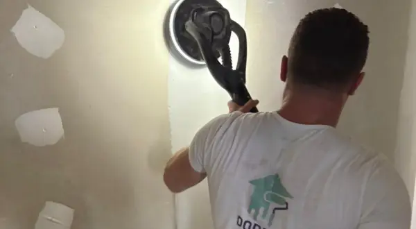 Un artisan utilise une ponceuse girafe pour lisser un mur en placo. C'est la ponceuse idéale pour un travail de finition impeccable.