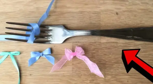En gaffel används för att knyta rosett med blått band. Små rosetter i mintgrönt, ljusblått och rosa ligger på träbordet.