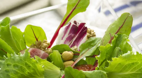 Ensalada fresca con brotes tiernos, nueces y trozos de jamón.