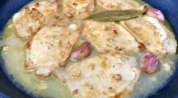 Filetes de lomo al ajillo dorándose en una sartén con ajo y laurel.