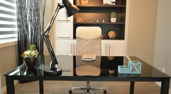 Nowoczesne biuro inspiracje: czarne biurko, wygodny fotel, lampa i regał pełen książek i dekoracji.