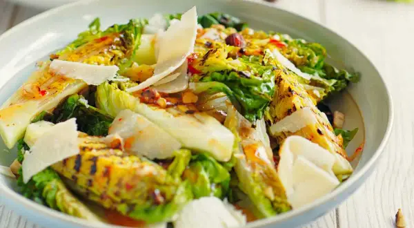 Deliciosa ensalada de cogollos a la parrilla, cubierta con lascas de queso parmesano y un aderezo vibrante.