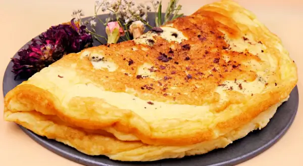 Puszysty omlet dla niemowlaka, delikatnie przyrumieniony, z ozdobnymi suszonymi kwiatami na talerzu.