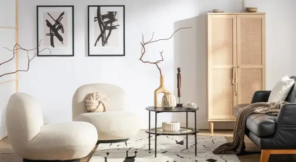 Przytulny salon w stylu hygge wnętrza. Jasne fotele, czarna skórzana kanapa, drewniana szafka z rattanowymi drzwiczkami i abstrakcyjne obrazy tworzą ciepłą atmosferę.