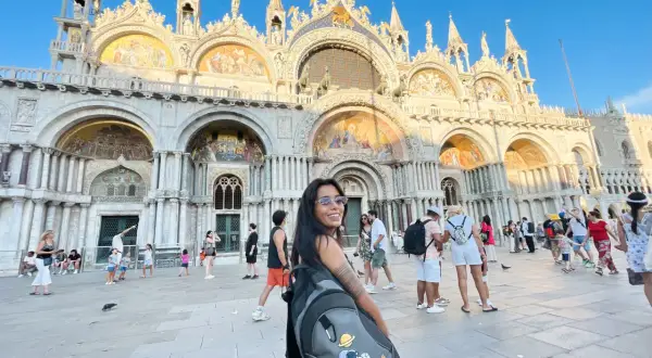 Una turista sorride davanti al magnifico museo San Marco di Venezia, con la sua architettura dorata e mosaici scintillanti.