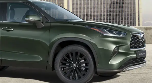 Zielony Toyota Highlander z czarnymi felgami stoi przed nowoczesnym budynkiem.
